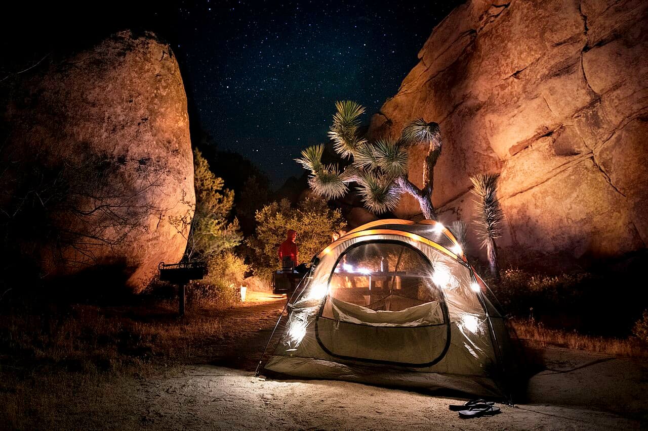 Campers gathered around a campfire with a tent among boulders at Joshua Tree National Park.